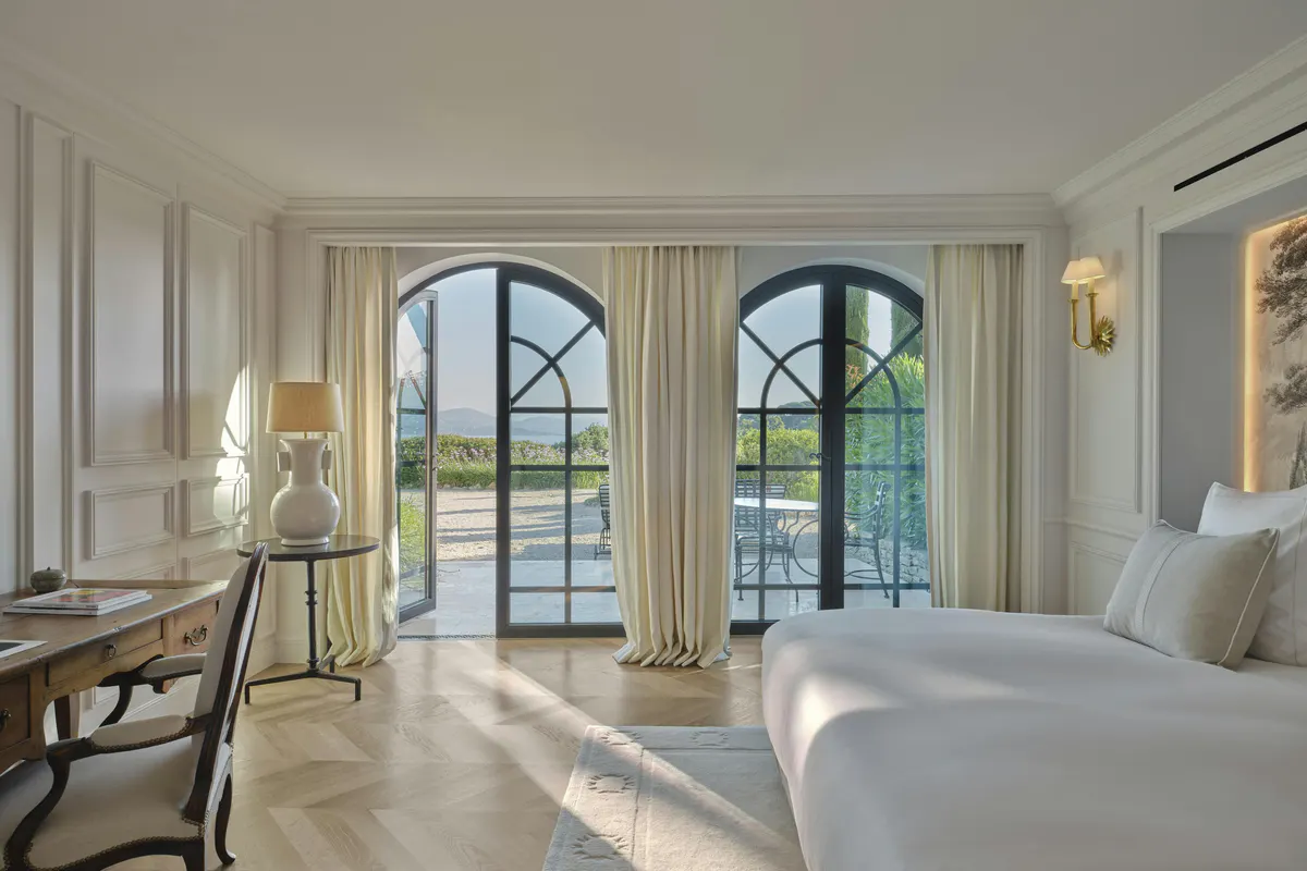 Bright bedroom with white furnishings, tall doors opening onto a bay-view terrace