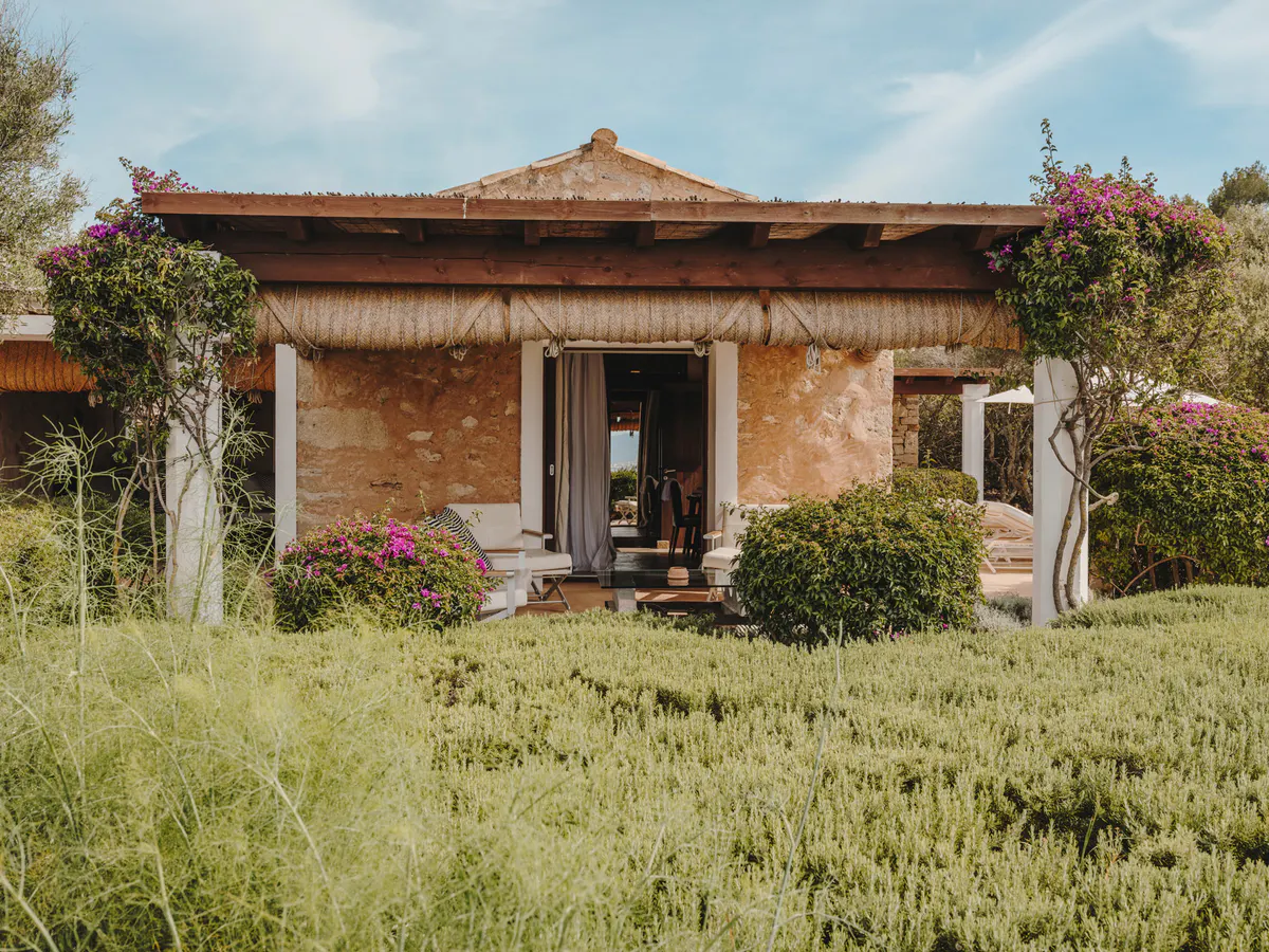 A terracotta pavilion with white columns and thatch roof, ringed by magenta bougainvillea and Mediterranean greenery