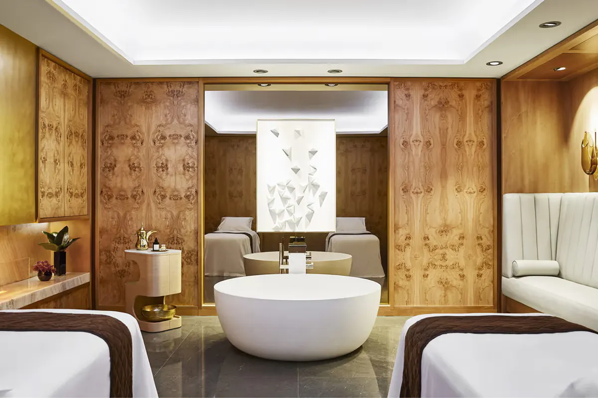 Spa treatment room with round marble tub, warm wood paneling, and cream leather seating
