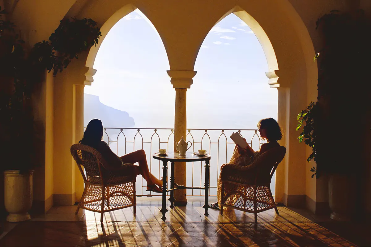 Silhouetted couple seated beneath Moorish arches with sea vista framed by columns at golden hour