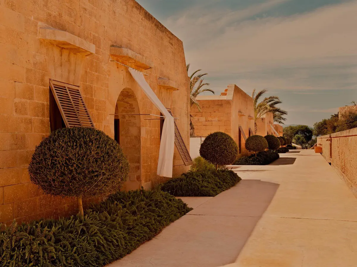 A fortification walkway lined with terracotta walls, topiary, and golden hour light