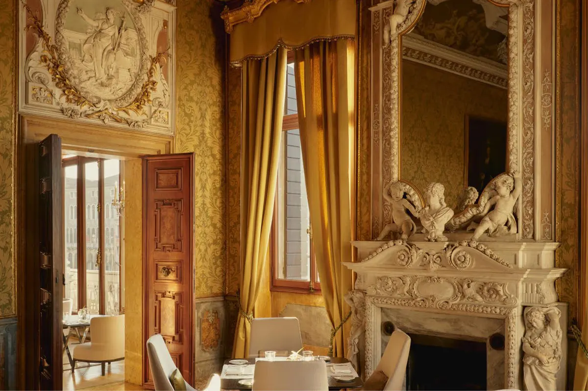 A corridor with mustard-colored walls, ornate gold-framed mirror, and sculptural white plaster details above doorways