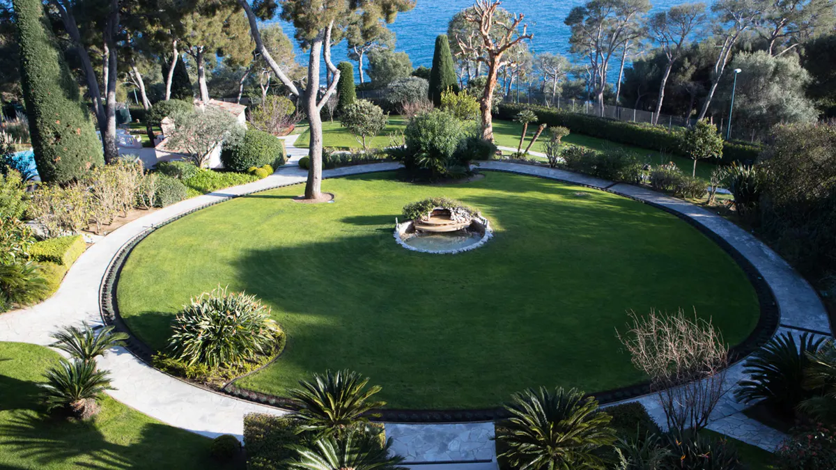 Circular lawn with central fire pit, trees, and sea view beyond