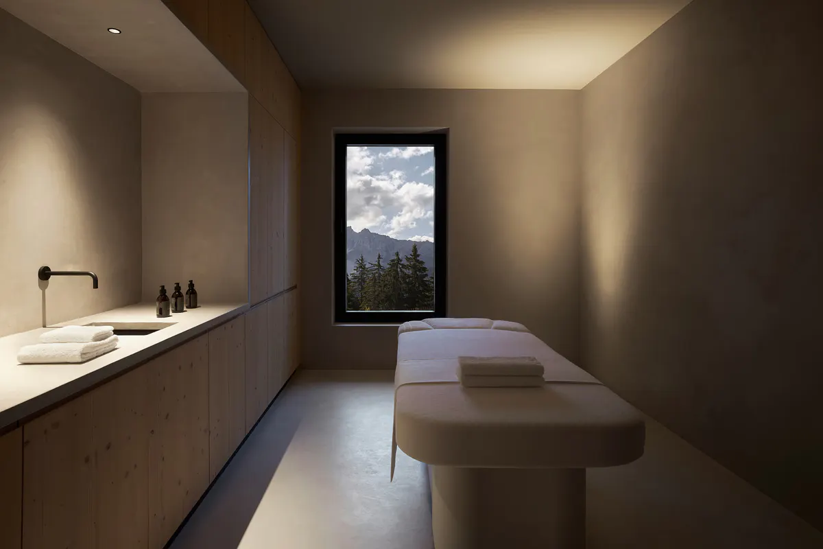 A massage or treatment room with light wood finishes, a treatment bench, and a framed window view
