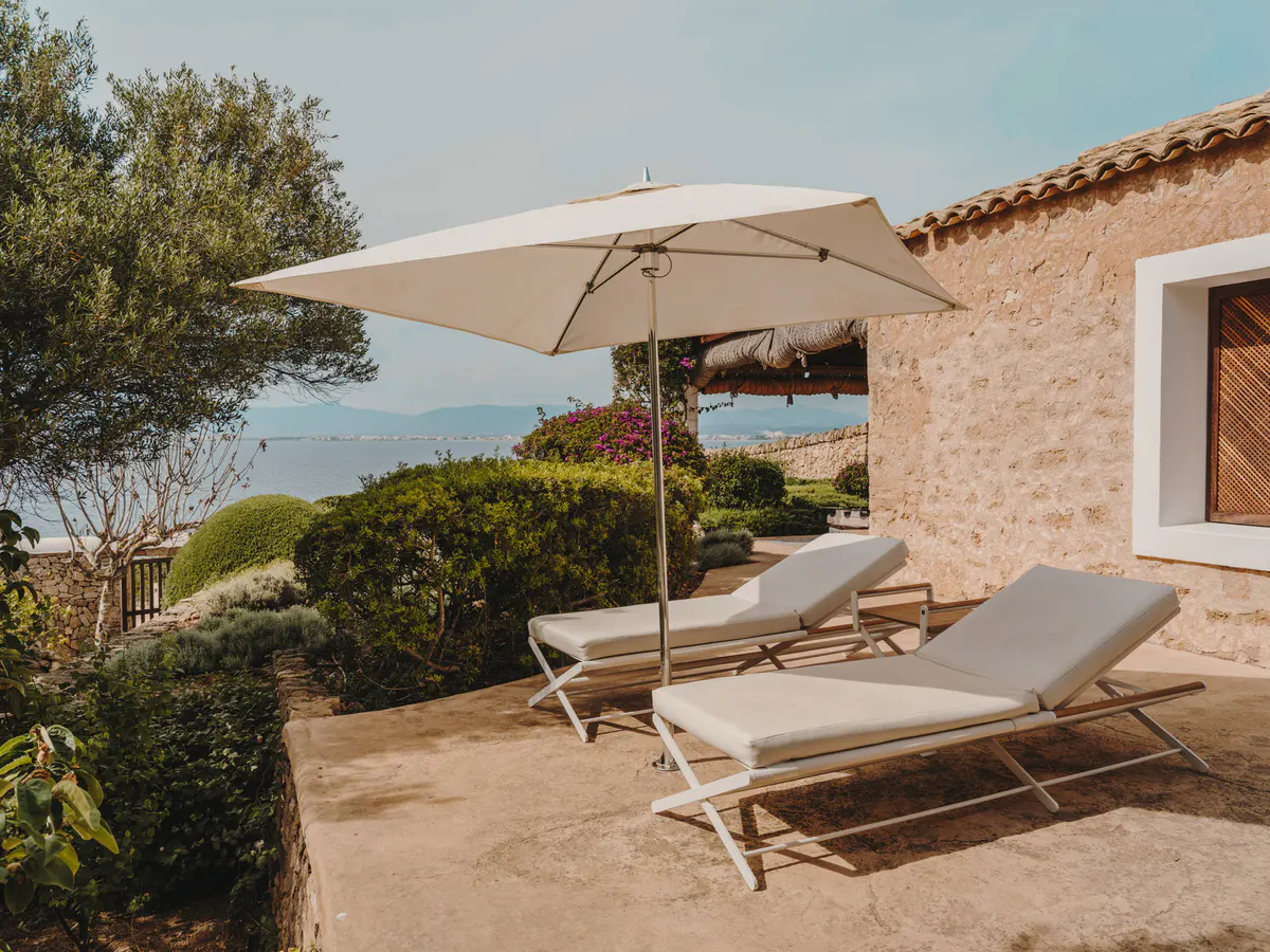 Two cream lounges beneath a square parasol overlook the Bay of Palma, with magenta bougainvillea and stone walls