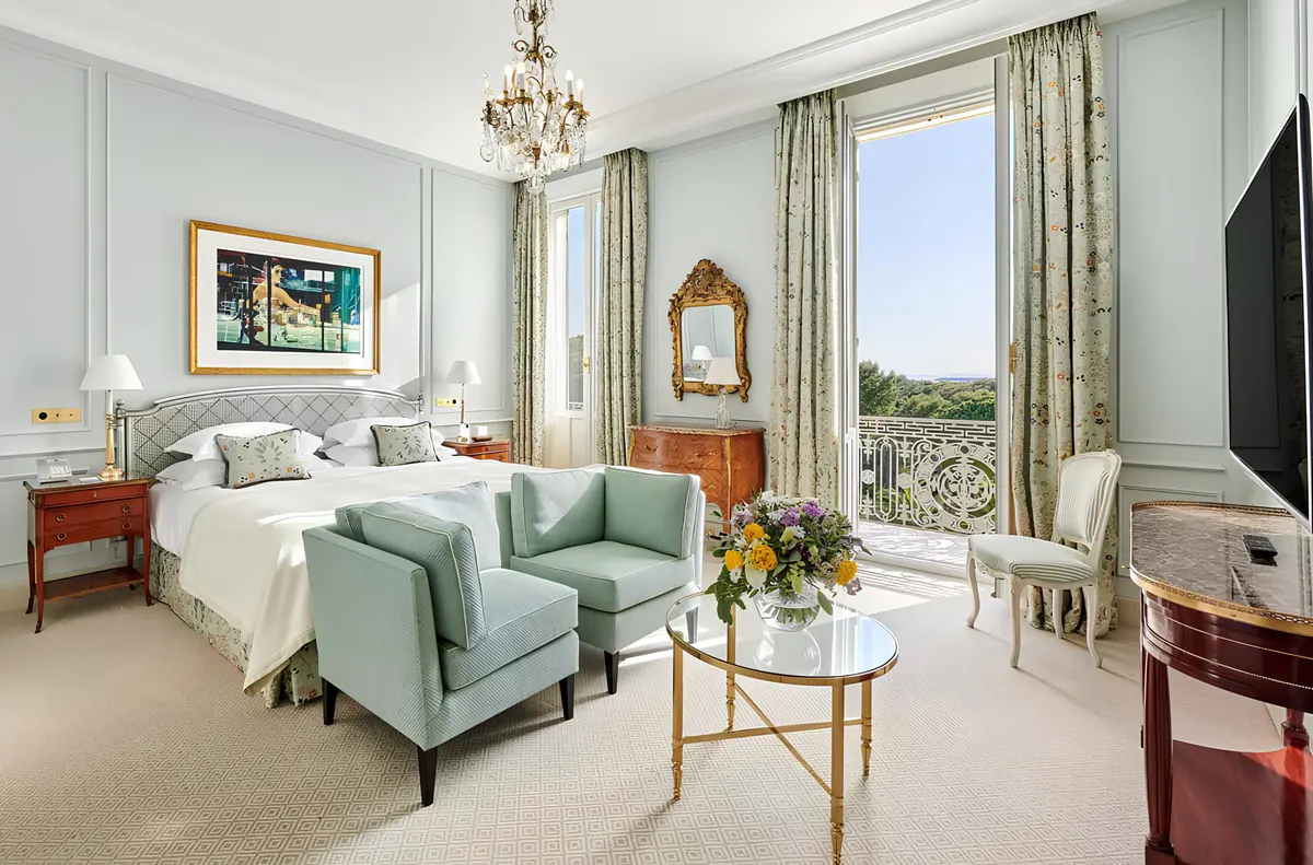 A suite with white marble furniture, light walls, patterned curtains, and views over the grounds
