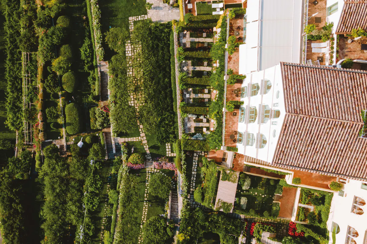 Aerial view of terraced palazzo with striped gardens, pathways, and Mediterranean coastline