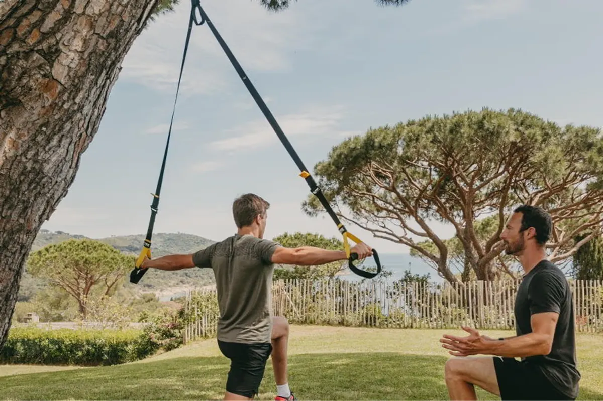 Two people doing suspension training exercises under large tree