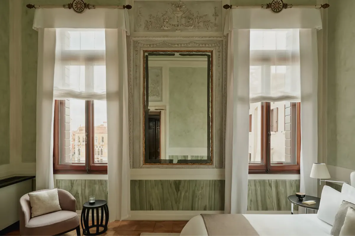 A light-filled room with pale green walls, arched windows, dark-framed mirrors, and cream drapery