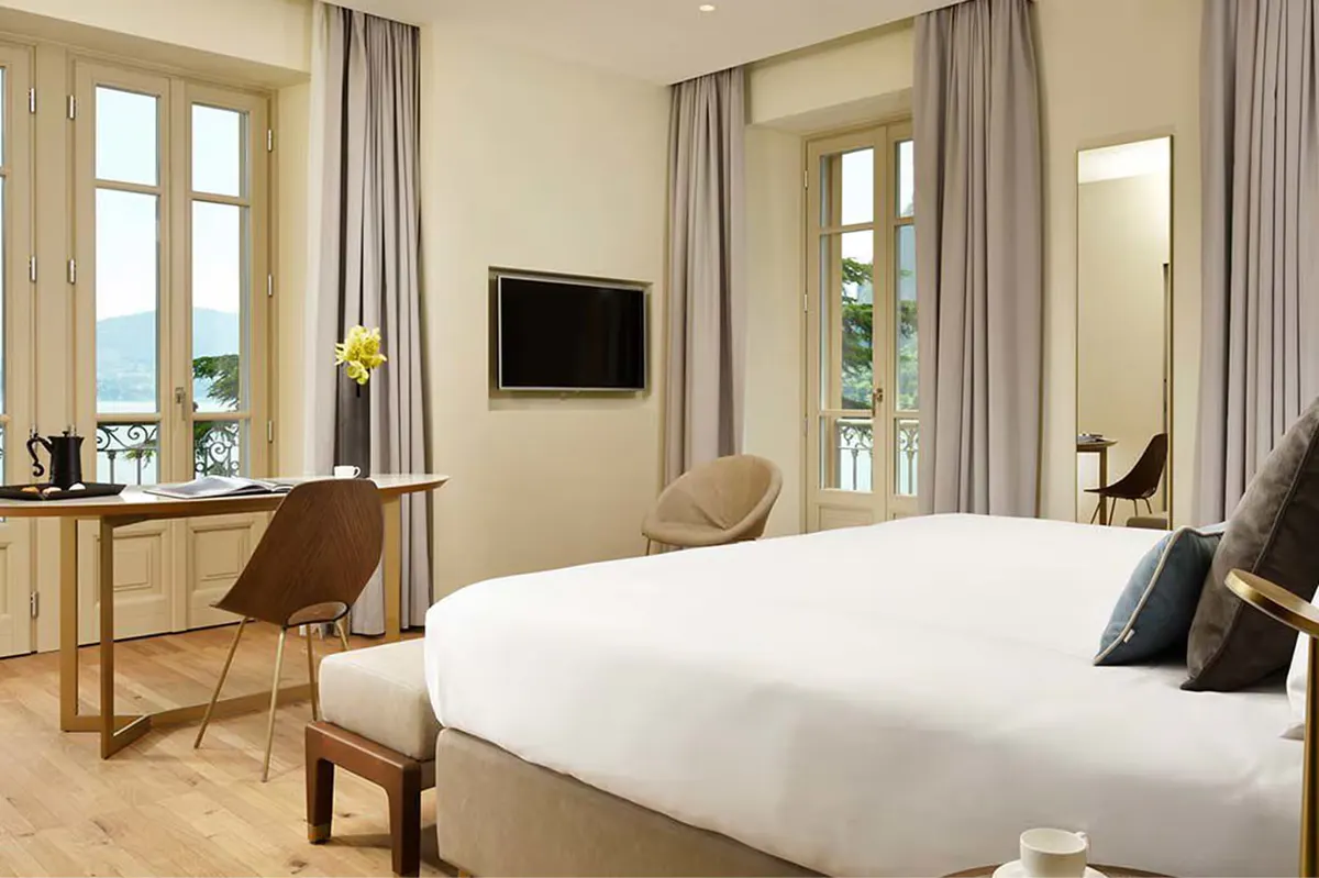A spacious bedroom with light wood floors, large windows, and a desk