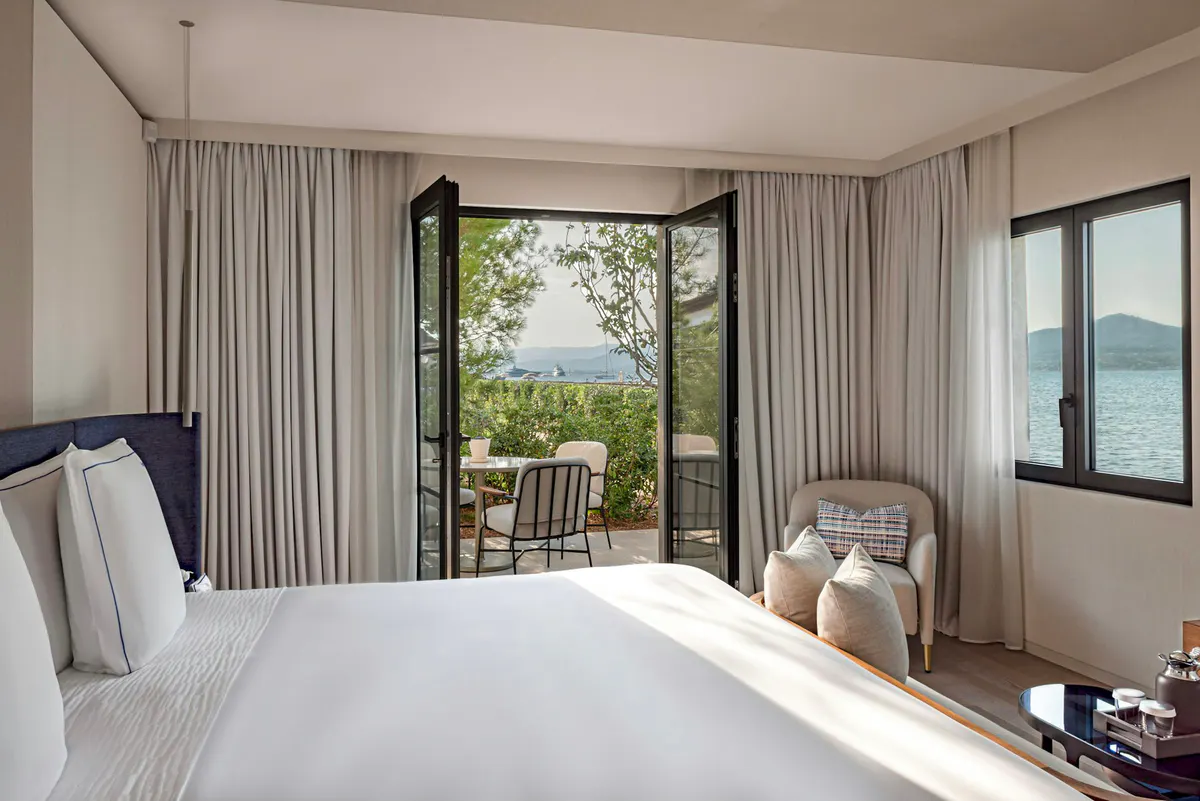 Bedroom with white bed and terrace opening to water views