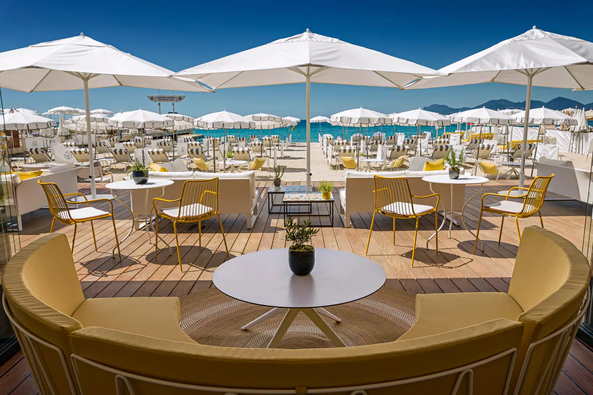 Beach club seating area with round tables under white umbrellas and clear blue sky above