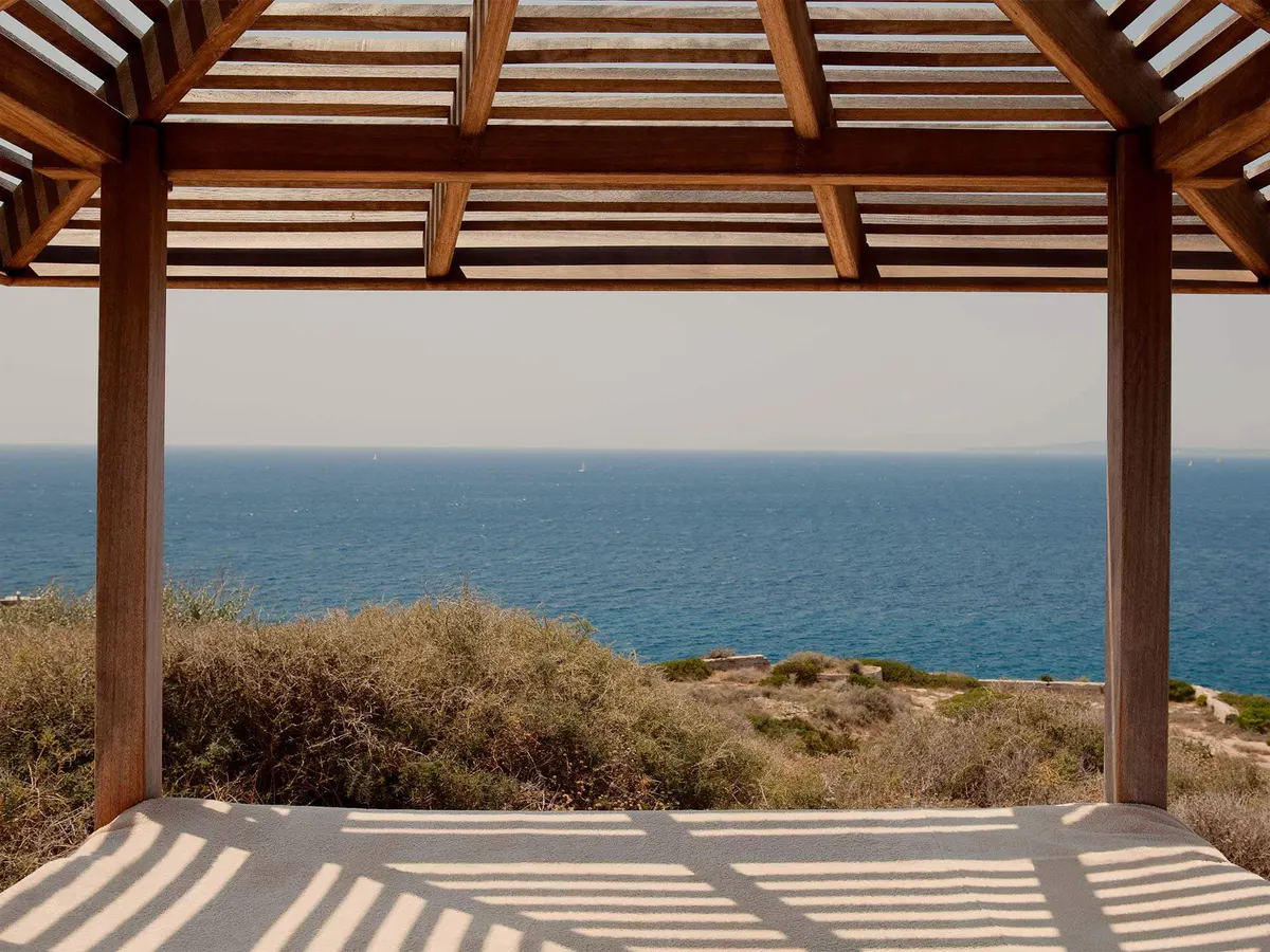 A bed with sheer cream curtains, wooden ceiling beams, and a window framing the sea