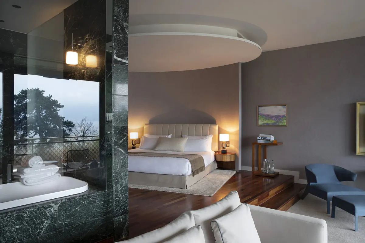 Contemporary bedroom with curved ceiling detail, pendant lighting, and sitting area
