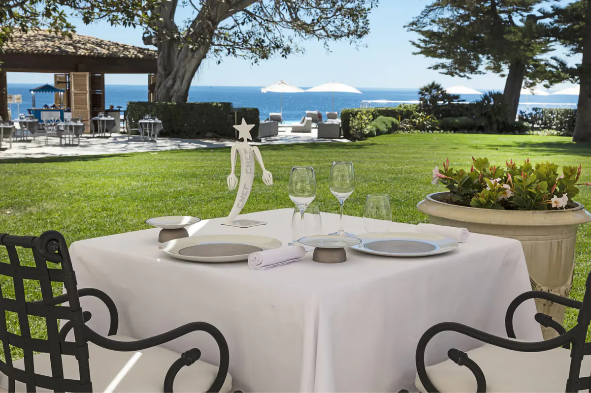 A round dining table under ancient trees with sea views beyond