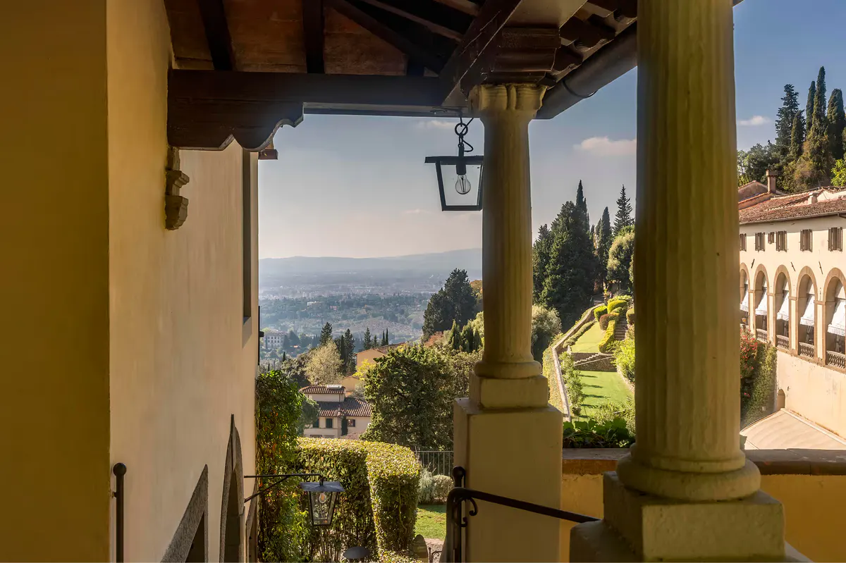 A columned terrace with morning light, marble columns, and distant views of Tuscany below