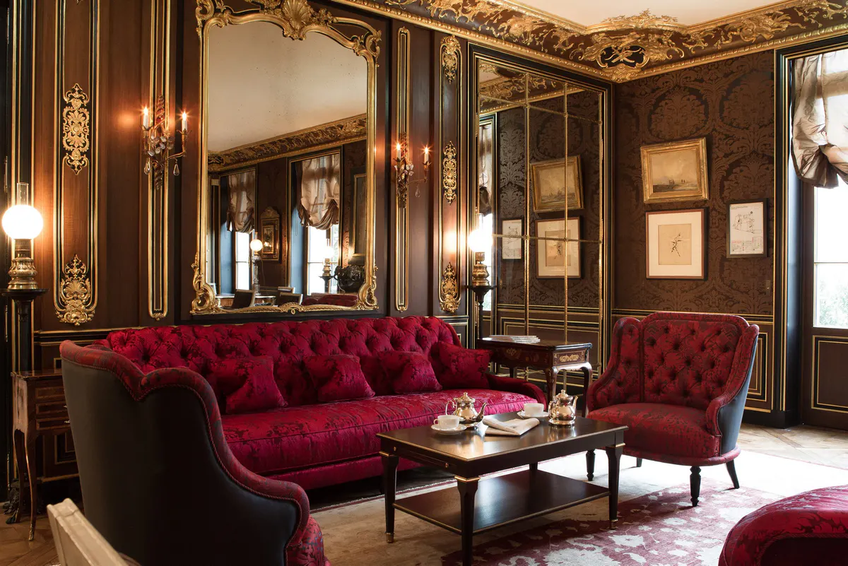 A formal living room with burgundy seating, gold paneling, and black marble accents