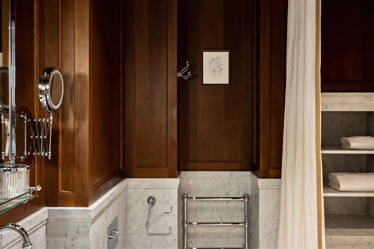 A marble bathroom with dark wood paneling and a modern circular mirror
