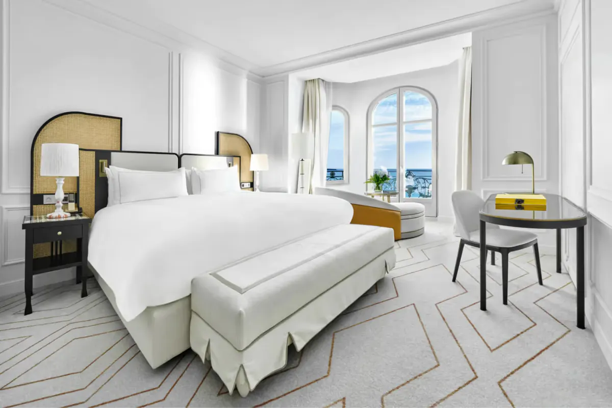 Guest room with white bed, brass-trimmed nightstands, and glass doors opening to a sea-view terrace