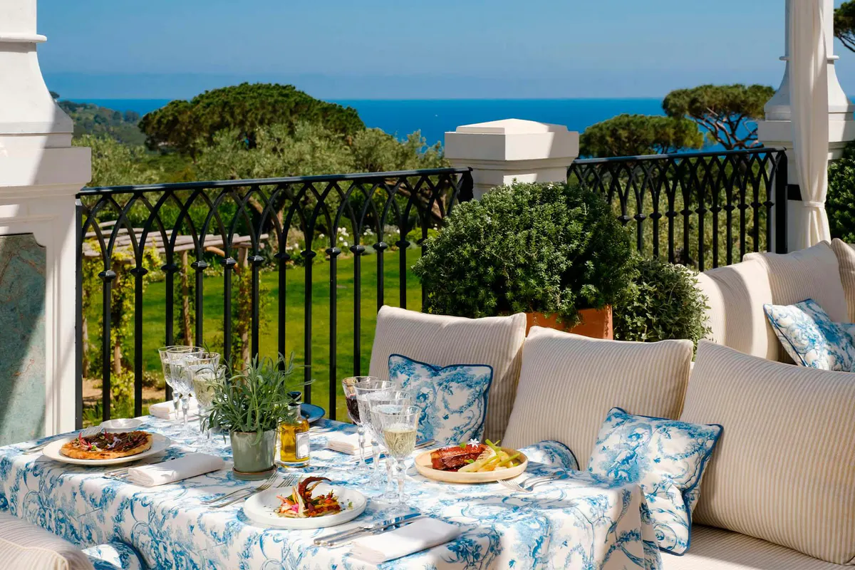 Covered terrace overlooking sea and forest with dining setup and blue-patterned cushions