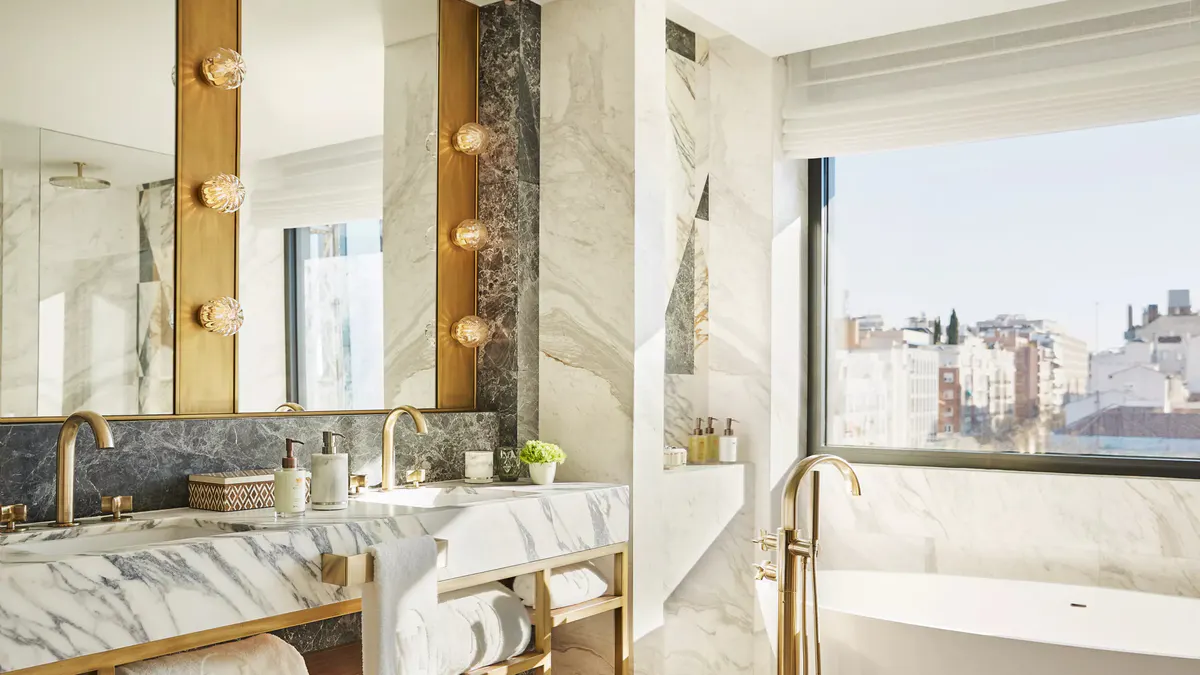 A bathroom vanity with gold mirror frame, marble countertop, and windows with city views