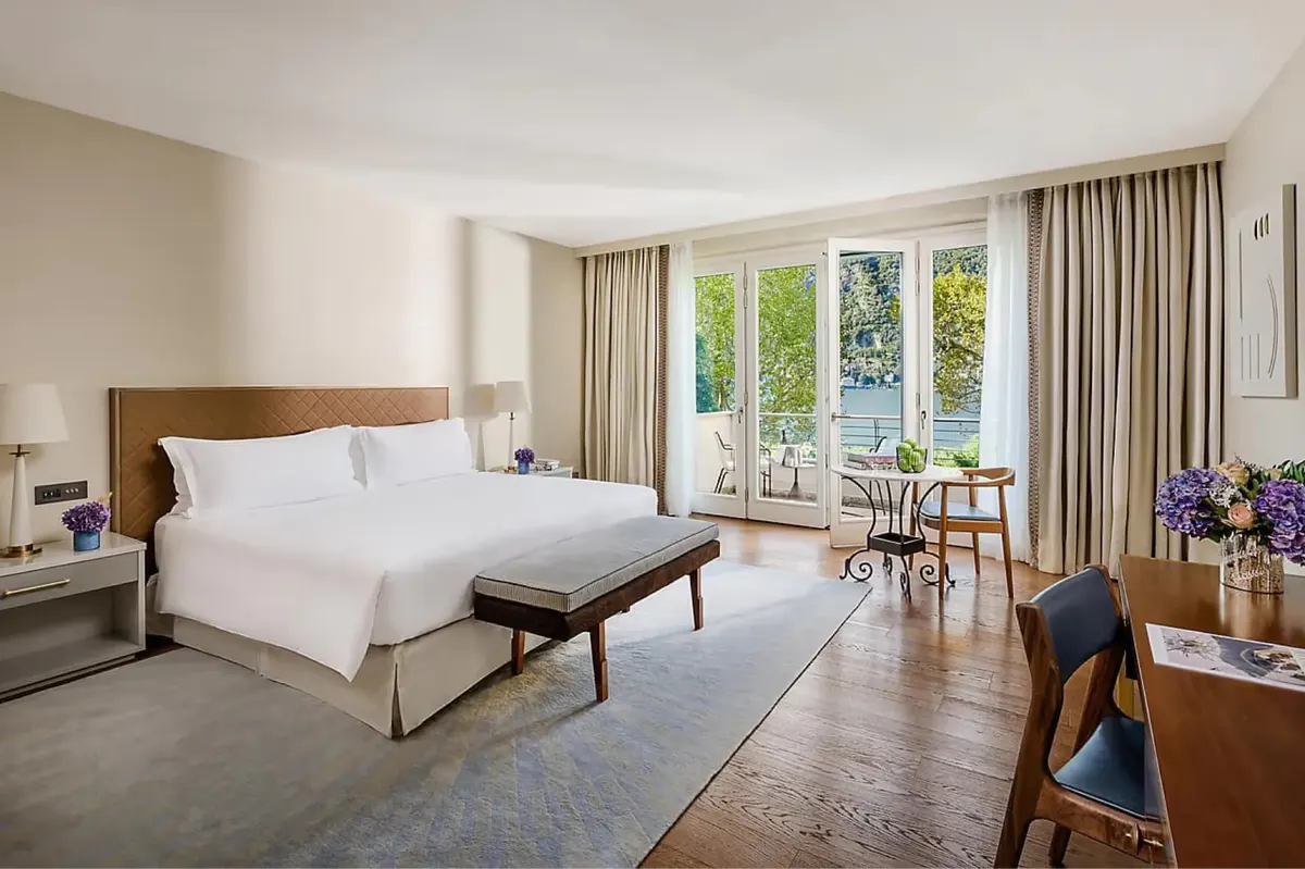 Bedroom with white linens and wood accents opening to views of mountains and water