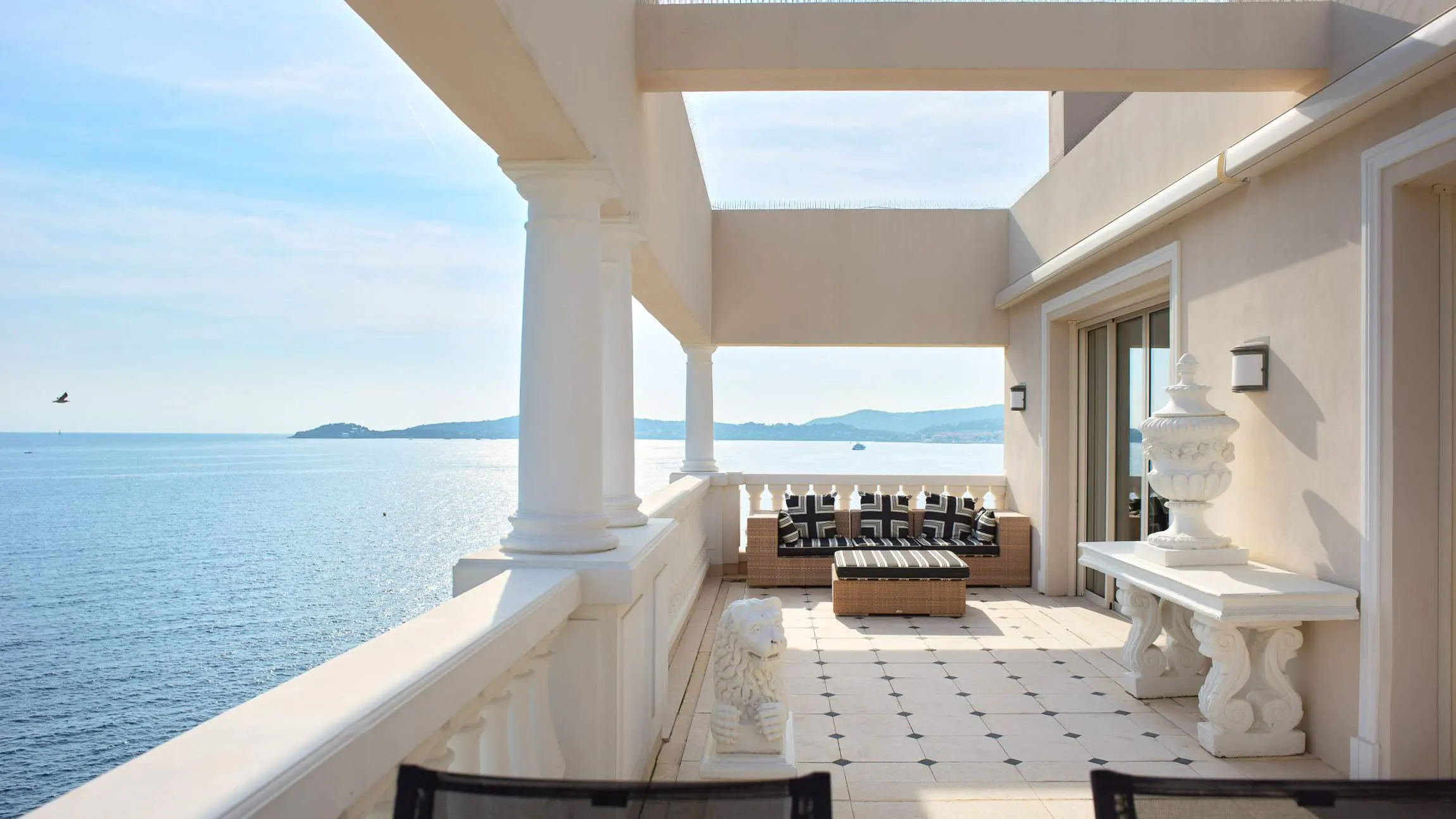 A modernist terrace with white columns overlooks calm Mediterranean waters