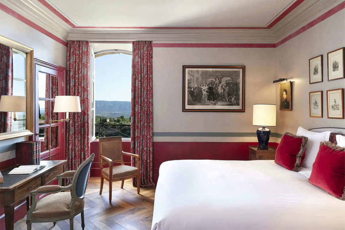 Bedroom with burgundy trim, draped curtains, white bedding, and valley views through French doors