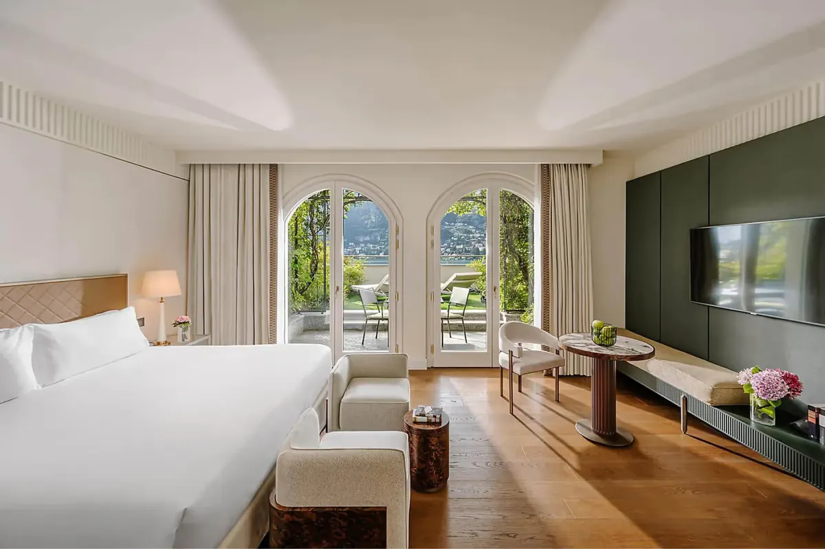 Spacious bedroom with white linens and views across French doors to mountains and lake