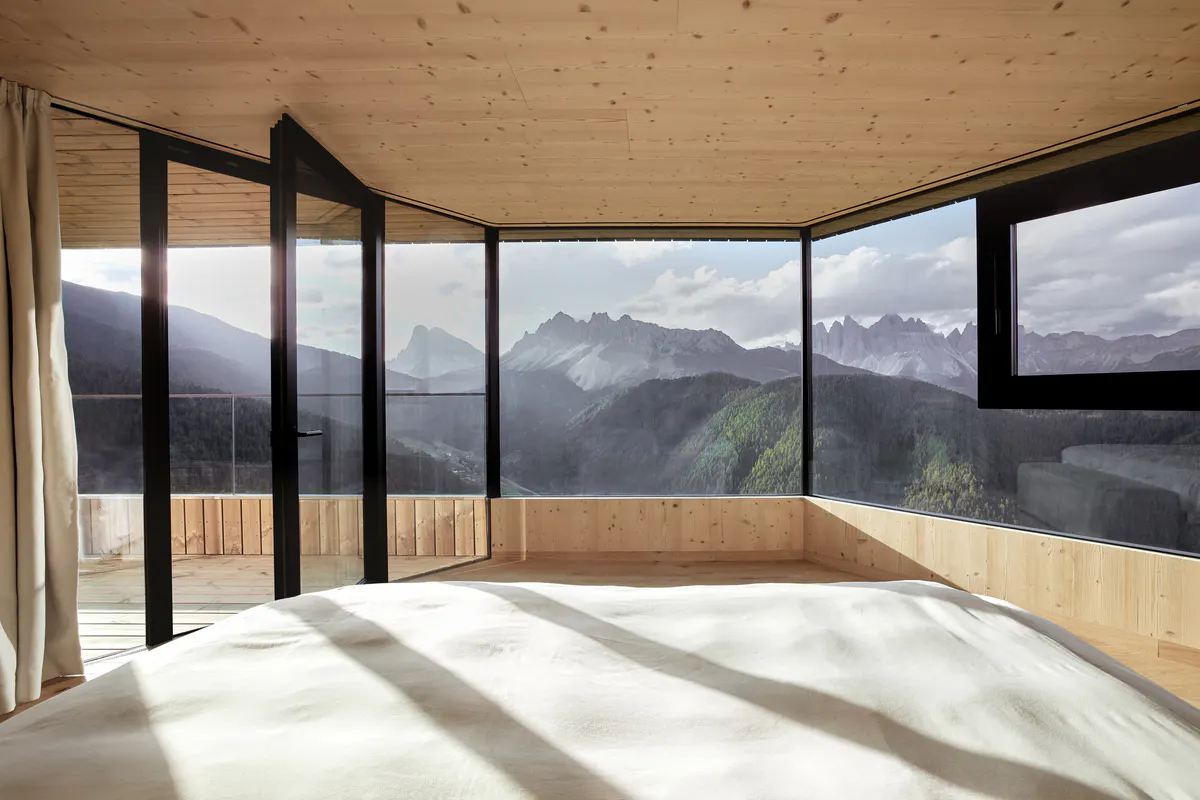A corner suite with wraparound black-framed windows, light wood finishes, and mountain landscape views