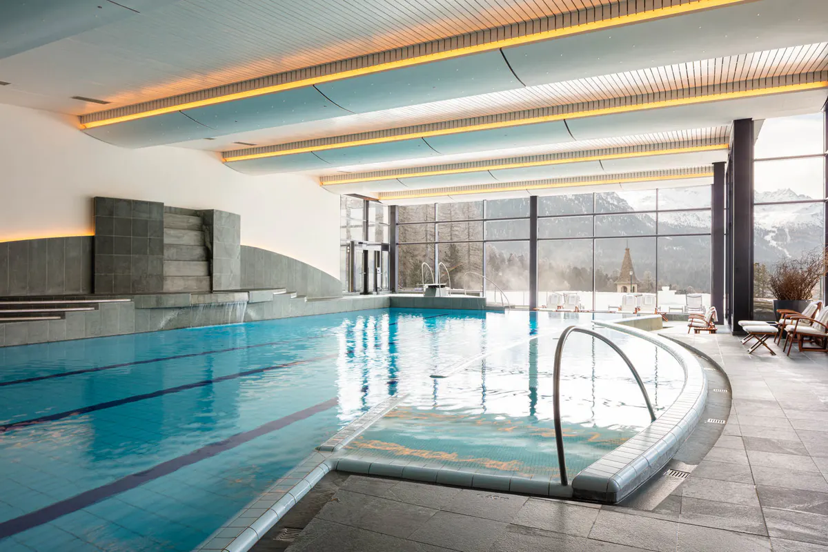 An indoor lap pool with large windows, integrated hot tub, and orange accent lighting