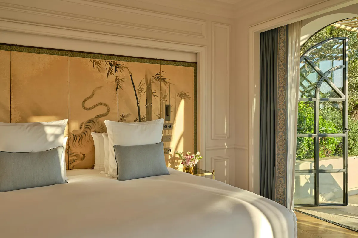 Bedroom with blue accent pillows, wooden finishes, and large glass doors to gardens