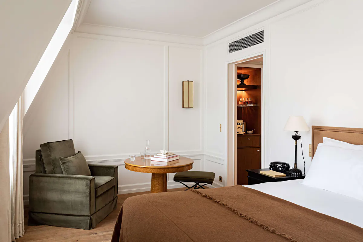A bedroom with pale walls, sloped ceiling, simple wood furniture, and natural light