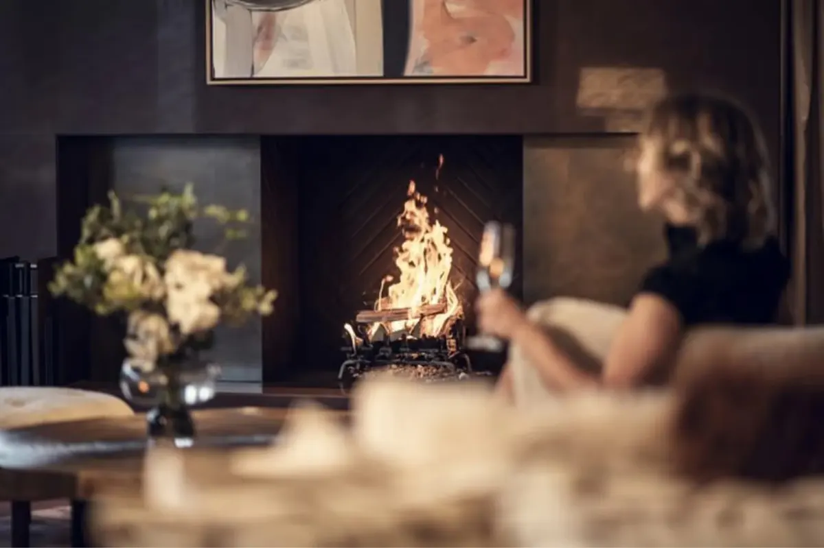A suite with a fireplace and upholstered seating framing snowy Alpine views