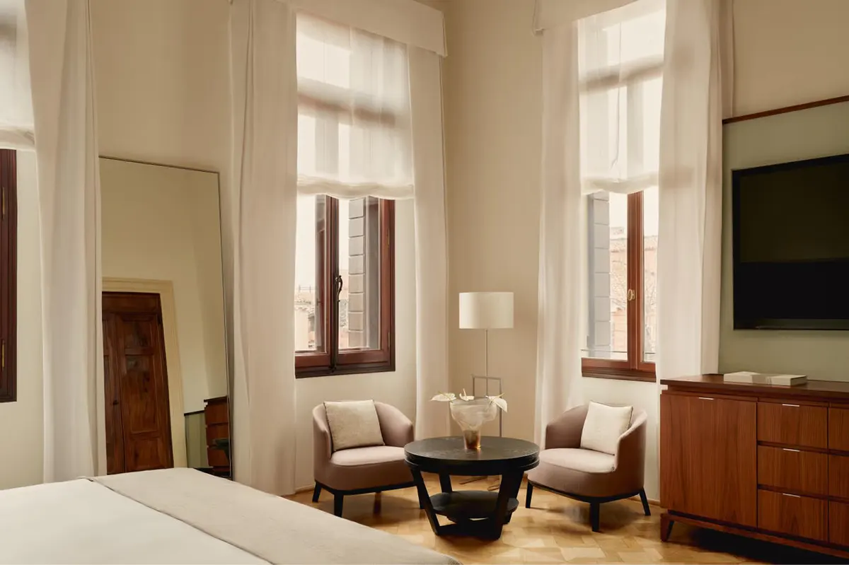 A room corner with high ceilings, tall windows, brown leather seating, and wooden flooring in warm tones