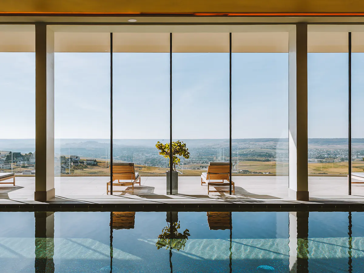 Indoor pool area with large windows overlooking vineyards and wooden lounge chairs
