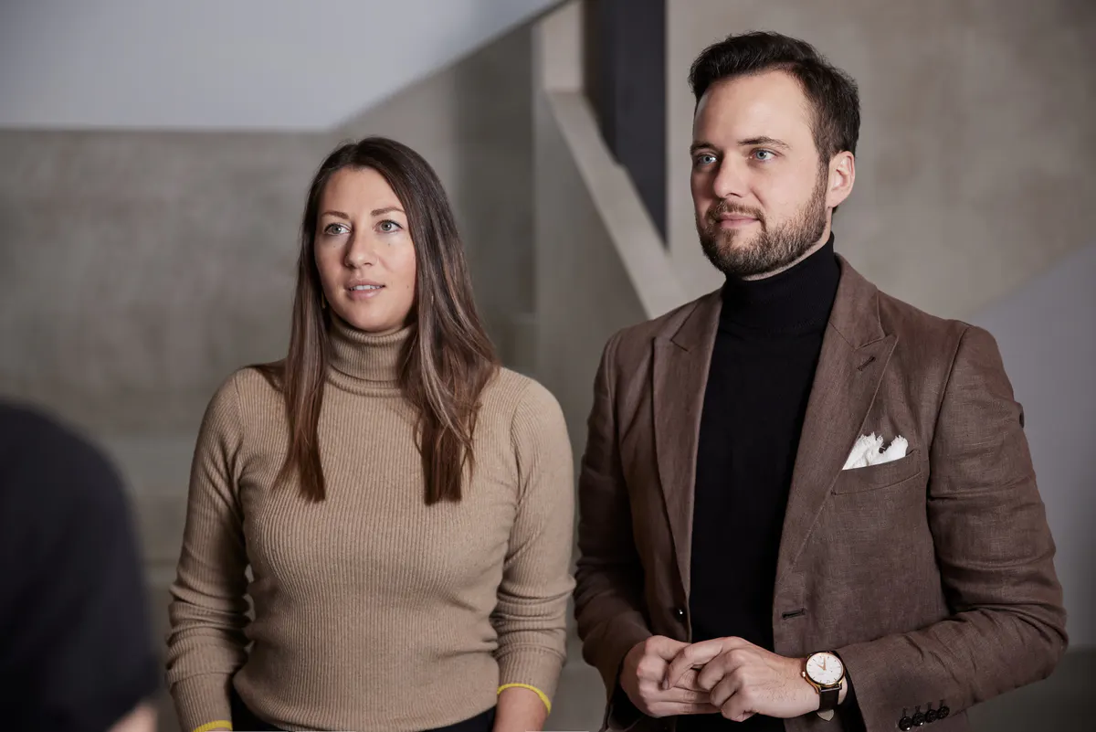 Two people standing in the hotel’s minimalist modern interior with neutral wall finishes visible behind