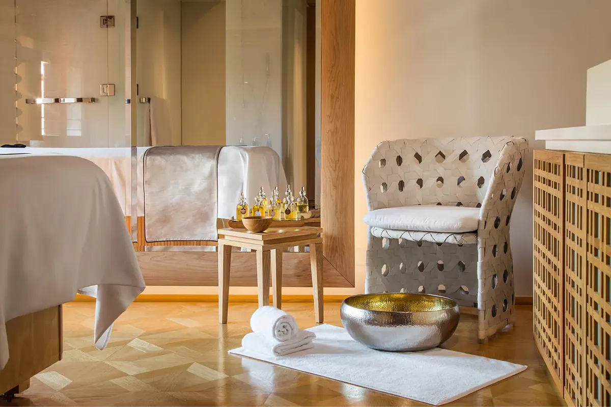 A spa treatment room with a massage table, wicker chair, natural lighting, and calm decor