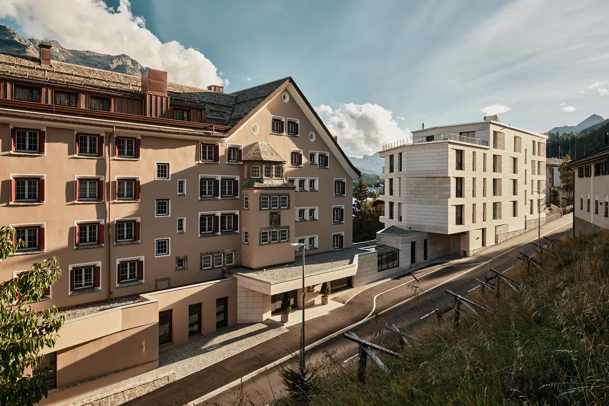 Historic stone buildings with modern glass addition and mountain backdrop in afternoon sun