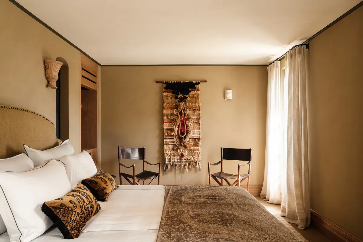 Ochre-toned bedroom with twin beds, patterned Berber pillows, woven textiles, rounded wooden doorway arch
