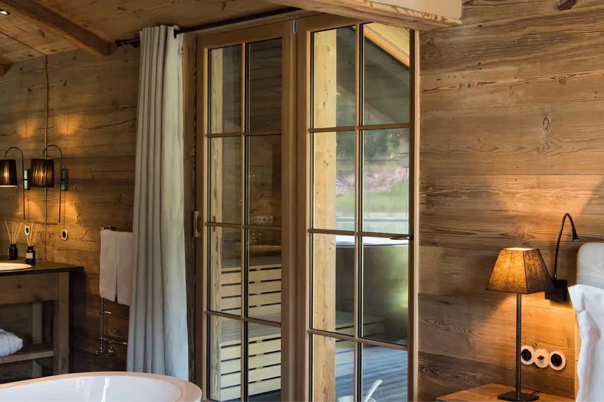 Wood-lined bedroom with glass partition walls and a freestanding tub