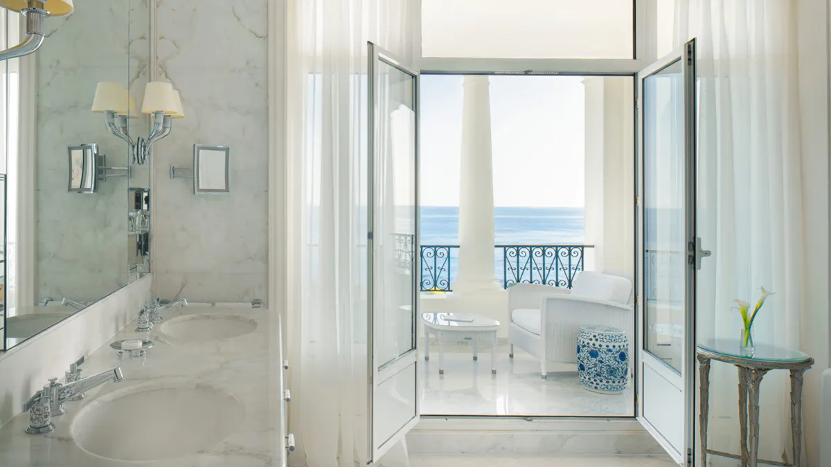 Spa-like marble bathroom with a soaking tub and sea view through glass doors