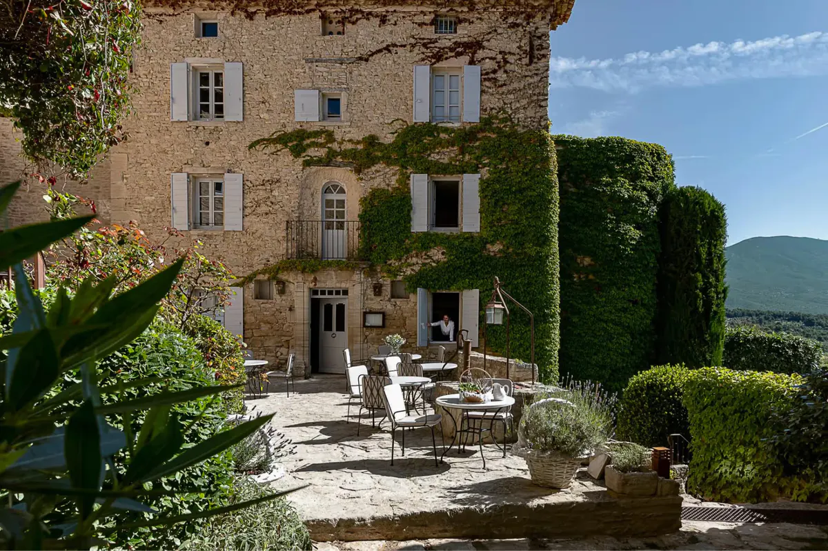 Stone village buildings with ivy, terrace furniture, and a clear mountain vista beyond