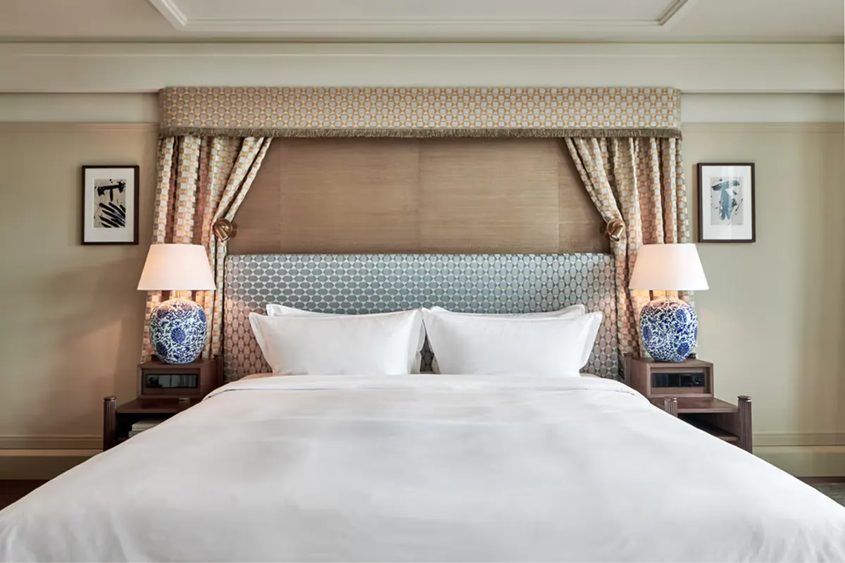 Bedroom with upholstered headboard, cream bedding, and patterned window curtains