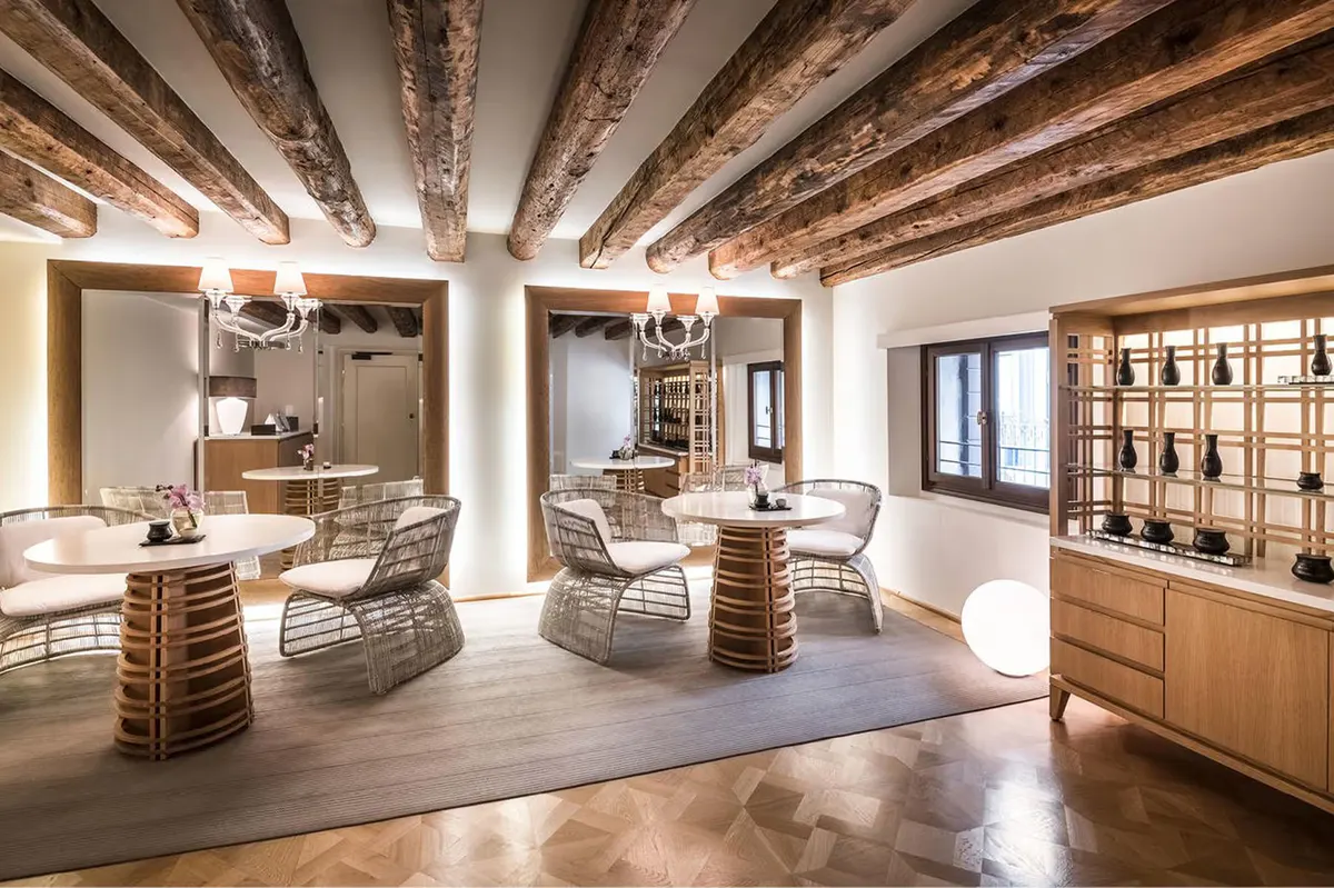A yoga studio with wooden beams, natural light, cream furnishings, and floor cushions