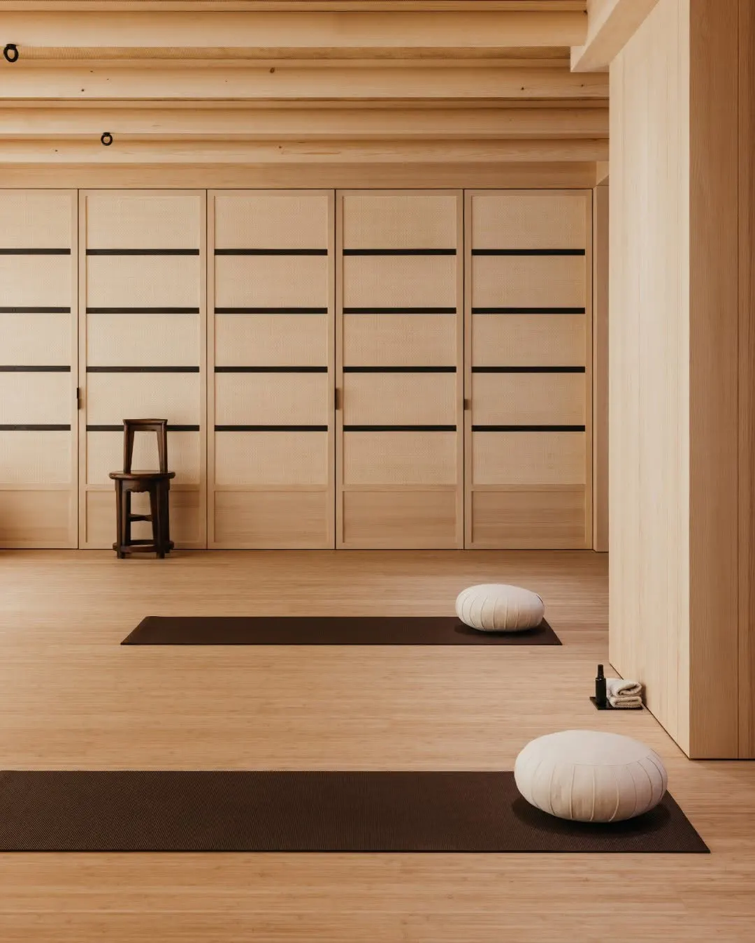Yoga studio with two floor cushions on mats, a wooden stool, and an exposed beam ceiling
