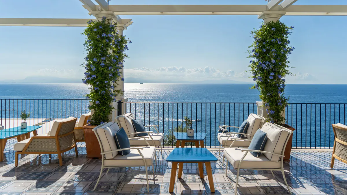 Covered terrace with comfortable seating, ivy-draped columns, and unobstructed sea views