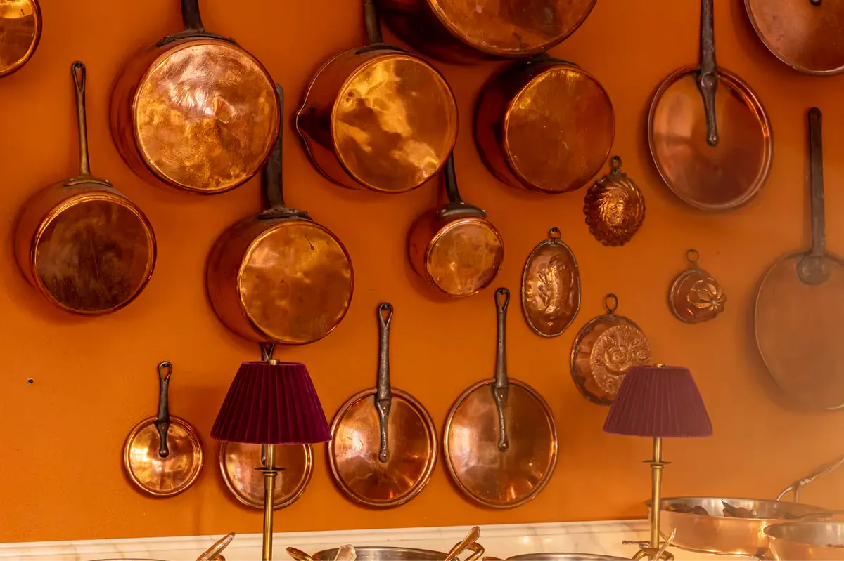 Hanging copper pots and pans displayed on a burnt-orange accent wall