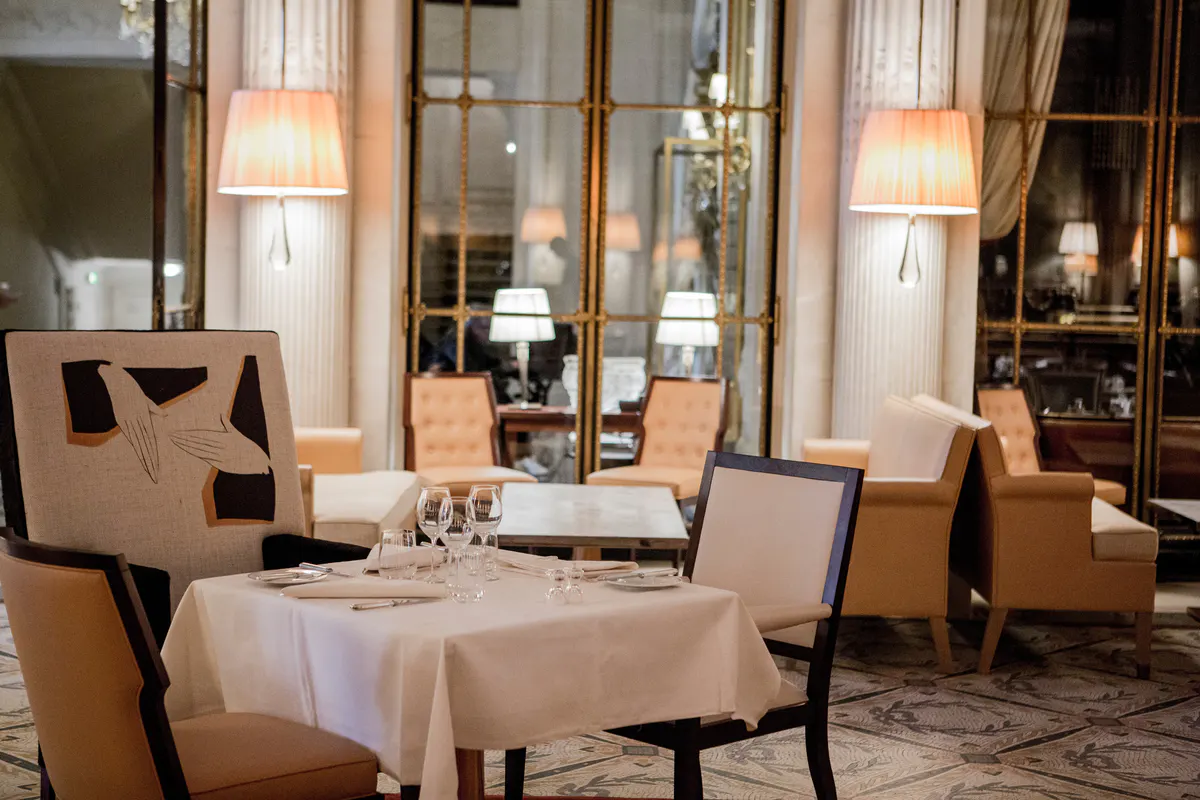 An intimate dining room with white tablecloths, classical furnishings, and soft warm lighting
