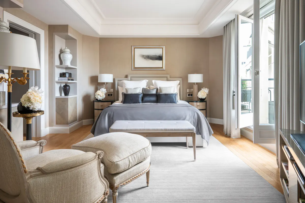 A spacious suite with light wood floors, white furnishings, and tall windows